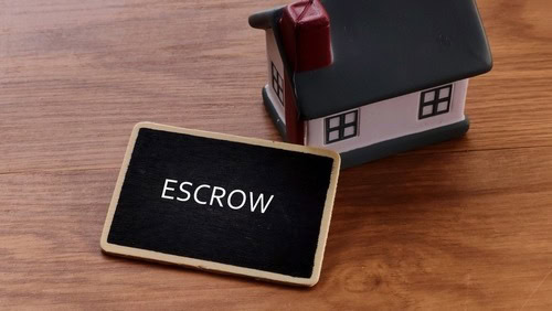 Small house model with escrow sign on wooden surface.