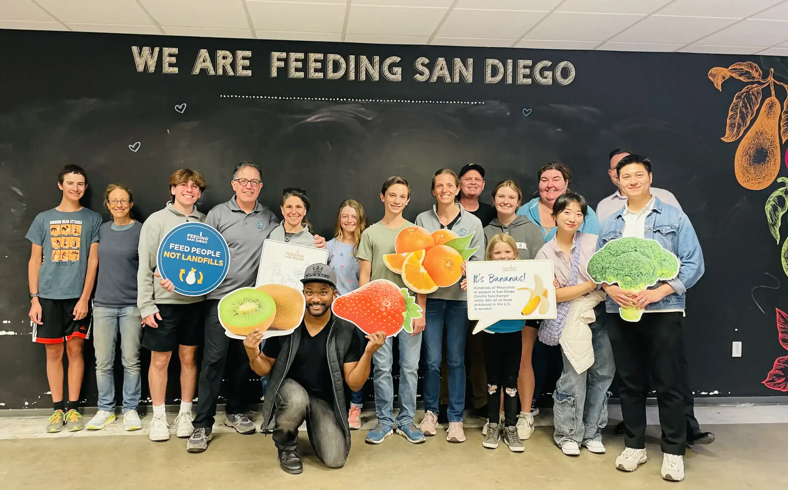 Group of volunteers holding fresh produce and food donations for San Diego feeding program.