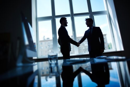 Two professionals shaking hands in a modern office with large windows.